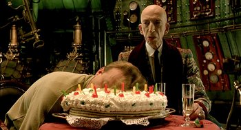Movie still from “The City of Lost Children” (1995), directed by Jean-Pierre Jeunet – A man and a woman sitting in front of a birthday cake; Medium shot, Over the shoulder angle