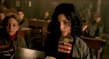 Movie still from “The City of Lost Children” (1995), directed by Jean-Pierre Jeunet – A young girl sitting at a table in front of a book; Close Up shot, Over the shoulder angle