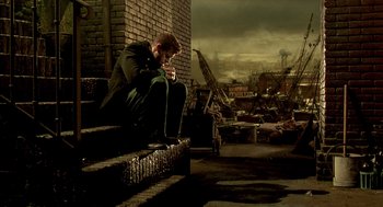 Movie still from “The City of Lost Children” (1995), directed by Jean-Pierre Jeunet – A man sitting on some steps looking down at his cell phone; Wide shot, High angle