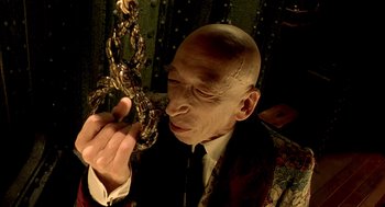 Movie still from “The City of Lost Children” (1995), directed by Jean-Pierre Jeunet – A man with bald head holding onto a chain; Close Up shot, High angle