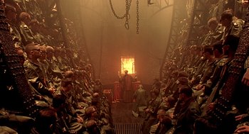 Movie still from “The City of Lost Children” (1995), directed by Jean-Pierre Jeunet – A group of people sitting in a large room; Extreme Wide shot, High angle