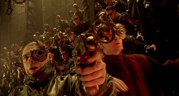 Movie still from “The City of Lost Children” (1995), directed by Jean-Pierre Jeunet – A group of people in a room holding a gun; Close Up shot, High angle
