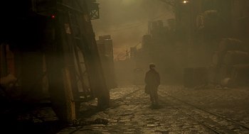 Movie still from “The City of Lost Children” (1995), directed by Jean-Pierre Jeunet – A person is walking down a street in the fog; Extreme Wide shot, High angle