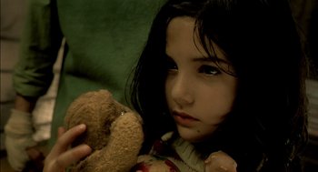 Movie still from “The City of Lost Children” (1995), directed by Jean-Pierre Jeunet – A young girl holding a teddy bear while sitting on a couch; Close Up shot, High angle