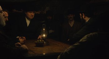 Movie still from “The Cobbler” (2014), directed by Tom McCarthy – A group of men sitting around a table with an oil lamp on it; Medium shot, Over the shoulder angle