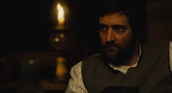 Movie still from “The Cobbler” (2014), directed by Tom McCarthy – A man with a beard wearing a vest and sitting in front of a lit candle; Close Up shot, Over the shoulder angle