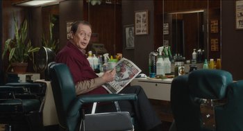 Movie still from “The Cobbler” (2014), directed by Tom McCarthy – A man sitting in a barber chair holding a magazine; Medium shot, Over the shoulder angle