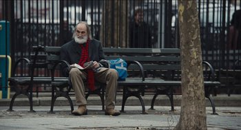 Movie still from “The Cobbler” (2014), directed by Tom McCarthy – An older man sitting on a bench reading a newspaper; Medium shot, Over the shoulder angle