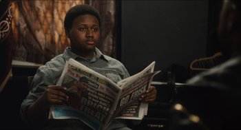 Movie still from “The Cobbler” (2014), directed by Tom McCarthy – A young man sitting down while reading a newspaper; Close Up shot, Over the shoulder angle