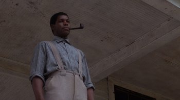 Movie still from “The Color Purple” (1985), directed by Steven Spielberg – A man with a pipe in his mouth standing under a ceiling; Medium shot, Low angle