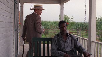 Movie still from “The Color Purple” (1985), directed by Steven Spielberg – Two men are sitting on a porch swing; Wide shot, Over the shoulder angle