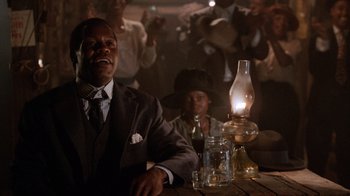 Movie still from “The Color Purple” (1985), directed by Steven Spielberg – A man sitting at a table with a woman standing next to him; Medium shot, Low angle