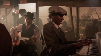 Movie still from “The Color Purple” (1985), directed by Steven Spielberg – A man in a suit and a hat playing a guitar; Medium shot, Over the shoulder angle