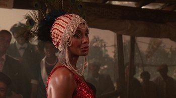 Movie still from “The Color Purple” (1985), directed by Steven Spielberg – A woman in a red and white dress with a peacock feather headpiece; Close Up shot, Over the shoulder angle