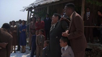 Movie still from “The Color Purple” (1985), directed by Steven Spielberg – A group of people standing in front of a building; Wide shot, Over the shoulder angle