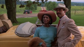 Movie still from “The Color Purple” (1985), directed by Steven Spielberg – A man and a woman standing next to each other in front of an antique car; Medium shot, Low angle