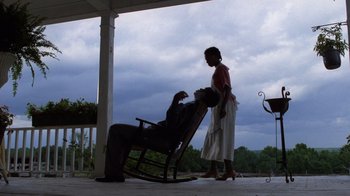 Movie still from “The Color Purple” (1985), directed by Steven Spielberg – A woman standing next to a man in a rocking chair on a porch; Wide shot, Low angle