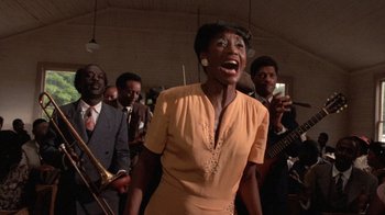 Movie still from “The Color Purple” (1985), directed by Steven Spielberg – A woman in a yellow dress is singing in front of a group of people; Medium shot, Low angle
