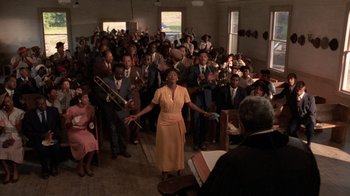 Movie still from “The Color Purple” (1985), directed by Steven Spielberg – A group of people in a room with a microphone; Extreme Wide shot, Low angle