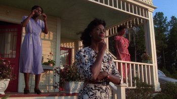 Movie still from “The Color Purple” (1985), directed by Steven Spielberg – A woman standing on the porch of a house with other women; Medium shot, Low angle