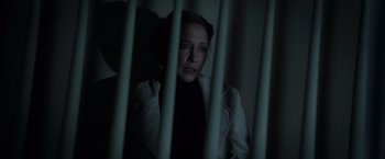 Movie still from “The Conjuring 2” (2016), directed by James Wan – A woman in a white jacket is looking through bars; Medium shot, High angle