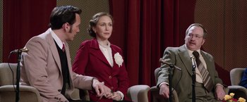 Movie still from “The Conjuring 2” (2016), directed by James Wan – A woman in a red jacket sitting next to two men; Medium shot, Over the shoulder angle