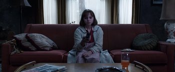 Movie still from “The Conjuring 2” (2016), directed by James Wan – A woman sitting on a couch holding a remote control; Medium shot, High angle