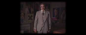 Movie still from “The Conjuring 2” (2016), directed by James Wan – An older man in a suit standing in front of a painting; Wide shot, High angle