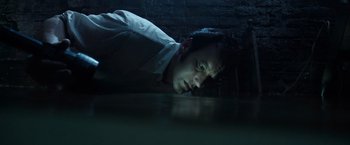 Movie still from “The Conjuring 2” (2016), directed by James Wan – A young man leaning on the ground in a dark room; Close Up shot, Overhead angle
