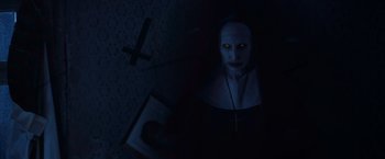 Movie still from “The Conjuring 2” (2016), directed by James Wan – A nun with yellow eyes is holding a book in a dark room; Close Up shot, High angle