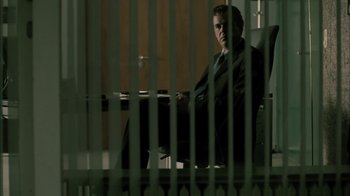 Movie still from “The Constant Gardener” (2005), directed by Fernando Meirelles – A man in a suit sitting in a chair in front of bars; Wide shot, Low angle