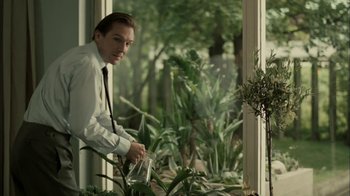 Movie still from “The Constant Gardener” (2005), directed by Fernando Meirelles – A man in a white dress shirt and a black neck tie is watering plants; Medium shot, Low angle