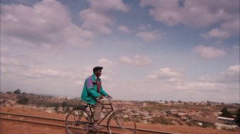 Movie still from “The Constant Gardener” (2005), directed by Fernando Meirelles – A man riding a bike on a dirt road; Extreme Wide shot, Low angle