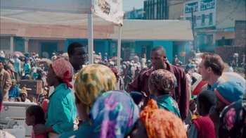 Movie still from “The Constant Gardener” (2005), directed by Fernando Meirelles – A group of people standing around a crowd of people; Wide shot, Over the shoulder angle