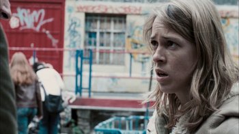 Movie still from “The Constant Gardener” (2005), directed by Fernando Meirelles – A young woman is standing in front of a building; Close Up shot, Over the shoulder angle