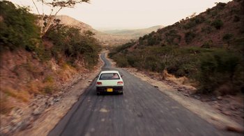 Movie still from “The Constant Gardener” (2005), directed by Fernando Meirelles – A car driving down a road in the middle of the day; Extreme Wide shot, High angle