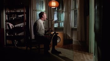 Movie still from “The Conversation” (1974), directed by Francis Ford Coppola – A man sitting on a chair playing a saxophone; Wide shot, High angle