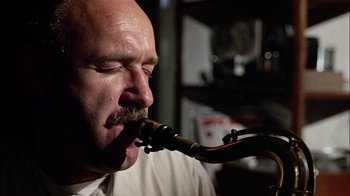 Movie still from “The Conversation” (1974), directed by Francis Ford Coppola – A man with a beard is playing a saxophone; Close Up shot, Low angle