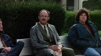 Movie still from “The Conversation” (1974), directed by Francis Ford Coppola – A man sitting on top of a bench holding a bag; Medium shot, Low angle