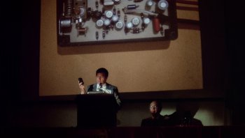 Movie still from “The Conversation” (1974), directed by Francis Ford Coppola – A man is giving a speech at a podium; Extreme Close Up shot, Low angle
