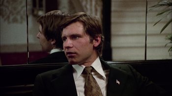 Movie still from “The Conversation” (1974), directed by Francis Ford Coppola – A man in a suit and tie sitting in a chair; Close Up shot, Over the shoulder angle