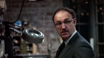 Movie still from “The Conversation” (1974), directed by Francis Ford Coppola – A man in a suit and tie standing in front of an object; Close Up shot, Low angle