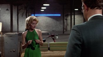 Movie still from “The Conversation” (1974), directed by Francis Ford Coppola – A woman in a green dress standing next to a fence; Medium shot, Over the shoulder angle