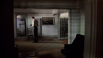 Movie still from “The Conversation” (1974), directed by Francis Ford Coppola – A man standing in a living room next to a chair; Wide shot, High angle
