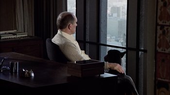 Movie still from “The Conversation” (1974), directed by Francis Ford Coppola – A man sitting in a chair next to a window with a black dog; Wide shot, Over the shoulder angle