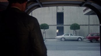 Movie still from “The Conversation” (1974), directed by Francis Ford Coppola – A car parked in front of a building on a rainy day; Wide shot, Over the shoulder angle