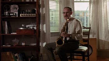 Movie still from “The Conversation” (1974), directed by Francis Ford Coppola – A man sitting on a chair holding a saxophone; Medium shot, Low angle