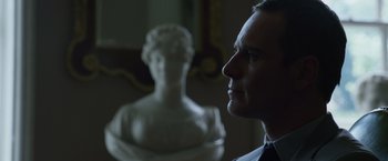 Movie still from “The Counselor” (2013), directed by Ridley Scott – A man standing in front of a bust of a woman; Close Up shot, Over the shoulder angle