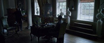 Movie still from “The Counselor” (2013), directed by Ridley Scott – A man sitting at a table in front of a painting; Wide shot, Over the shoulder angle