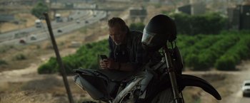 Movie still from “The Counselor” (2013), directed by Ridley Scott – A man sitting on top of a motorcycle looking at his cell phone; Medium shot, Low angle